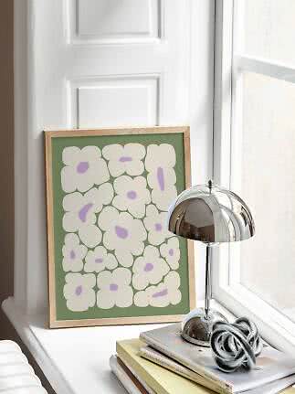Affiche florale encadrée avec fleurs blanches sur fond vert, sur un rebord de fenêtre près d'une lampe chromée