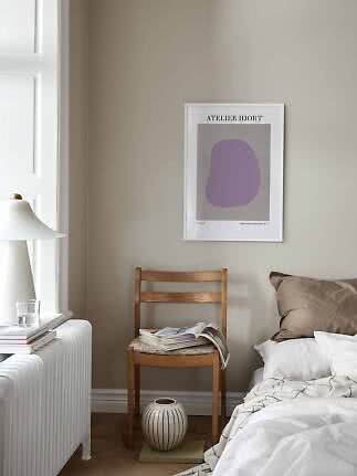 Schlafzimmerecke mit abstraktem Poster, Holzstuhl mit Magazin, weißem Bett und Lampe am Fenster