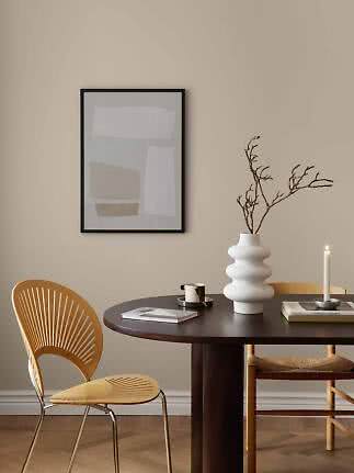 Abstrakt plakat i sort ramme over mørkt spisebord med hvid vase, gren, lys og stol