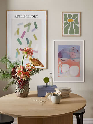 Tavolo da pranzo con composizione floreale, libri, tazza e tre stampe d’arte incorniciate