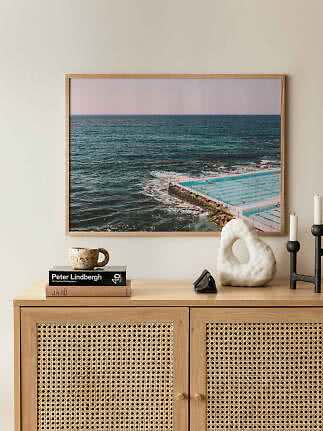 Indrammet havfoto med ocean pool over en træskænk med kop, bøger, skulptur og lysestager