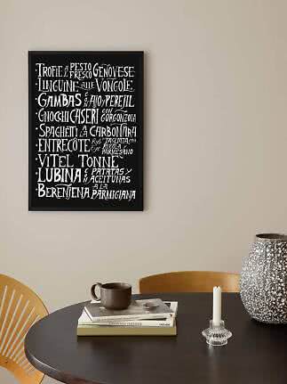 Affiche encadrée noire avec menu manuscrit blanc au-dessus d'une table ronde avec tasse et vase