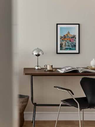Desk with chrome lamp, mug and open book beneath framed colorful harbor print