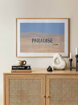 Framed desert landscape poster with the word "PARADISE" above a wooden cabinet.