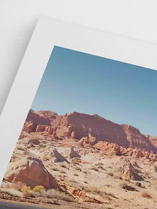 Close-up van een ingelijste woestijnlandschapprint met rode rotsen en blauwe lucht