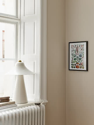 Botanisk plakat med grøntsager i sort ramme på beige væg ved vindue og hvid bordlampe