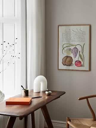 Gerahmter botanischer Druck über einem Holztisch am Fenster in hellem Interieur