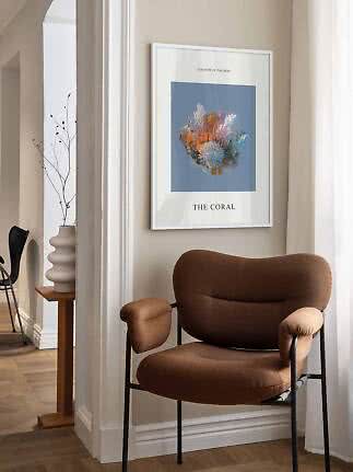 Indrammet koralplakat på beige væg over en brun lænestol ved et lyst vindue
