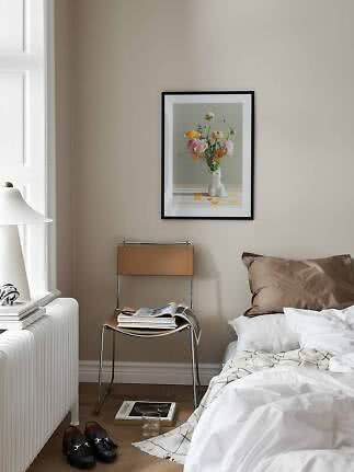 Camera da letto con letto, sedia e stampa floreale incorniciata su parete beige