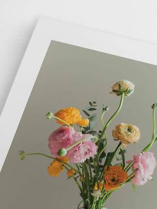 Bouquet colorato con ranuncoli rosa, gialli e color crema davanti a una parete chiara