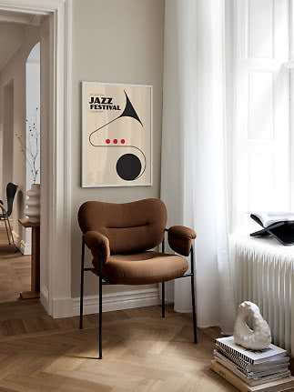 Brun polstret stol med sorte ben ved siden af et jazzfestival-print i et lyst hjørne
