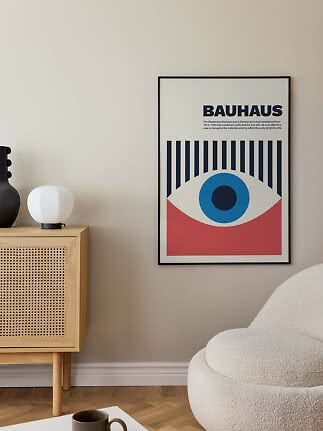 Indrammet Bauhaus-plakat med grafisk øje i blå, rød og sort på beige væg