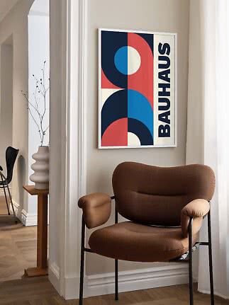 Abstrakt Bauhaus-plakat i hvid ramme over en brun lænestol i et lyst rum