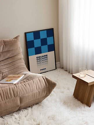 Gerahmtes blaues geometrisches Poster an der Wand neben Sessel und kleinem Holztisch