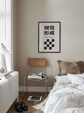 Minimalistisches Schlafzimmer mit Bett, Stuhl, Lampe und Schwarzweiß-Poster an beiger Wand
