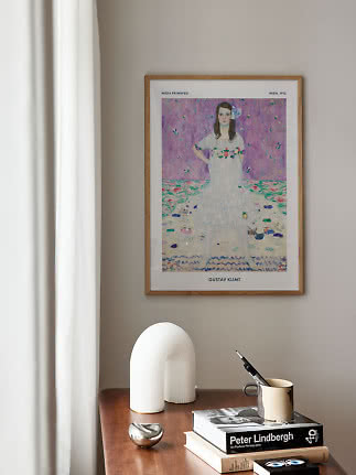 Inramad Gustav Klimt-affisch på beige vägg ovanför träbord med böcker, vas och mugg
