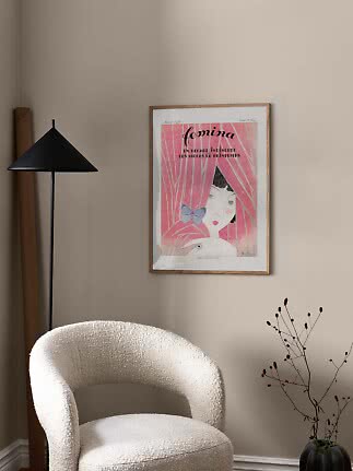 Framed pink art print on beige wall above a white armchair beside a black floor lamp