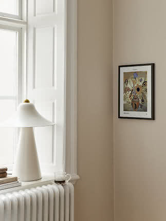 Minimalistische hoek met witte tafellamp op vensterbank en ingelijste kunstprint aan beige muur