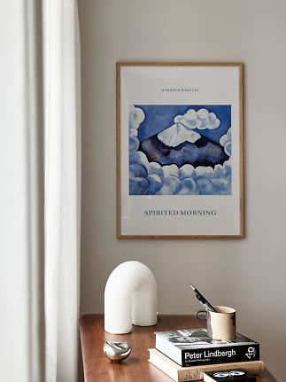 Póster enmarcado de Marsden Hartley sobre mesa de madera con libros, taza y objetos decorativos blancos