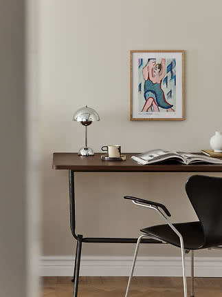 Mörkt träskrivbord med kromlampa, mugg, öppen bok och inramad konst på beige vägg