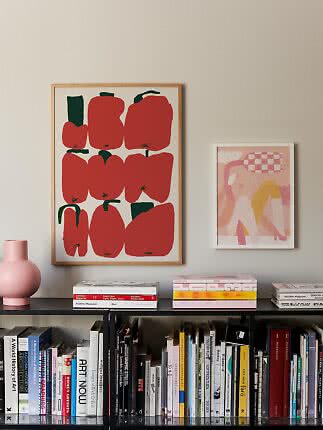 Bookshelf with art books, pink vase, and two framed prints on a beige wall