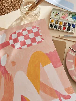 Painting table with abstract pink artwork, watercolor palette, brushes and glass jar of water