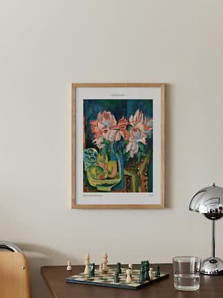 Indrammet kunstplakat med lyserøde blomster over et bord med skakbræt, glas og kromlampe