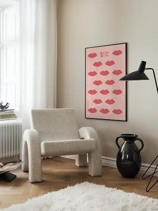 Rosa poster med röda läppar i svart ram ovanför en krämfärgad fåtölj.