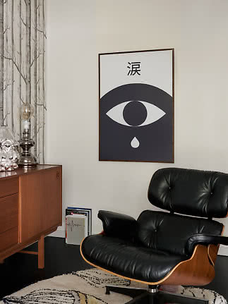 Gerahmtes schwarz-weißes Poster mit Auge und Träne über einem schwarzen Sessel