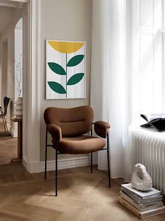 Brun polstret stol med sorte ben ved vindue under grafisk blomsterplakat