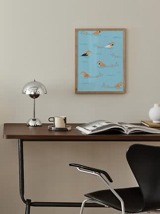 Framed blue swimmer print above a desk with lamp, mug, and open book