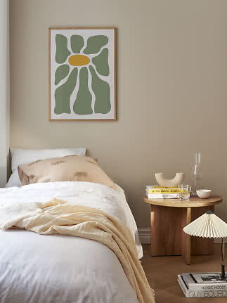 Chambre avec lit, table d’appoint ronde en bois et affiche fleur abstraite sur mur beige