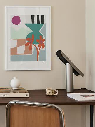 Affiche abstraite encadrée avec vase et fleurs au-dessus d’un bureau avec lampe et livres
