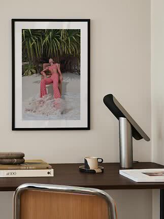 Framed art print of woman in patterned outfit on chair by water and tropical plants