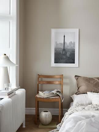 Schlafzimmer mit Bett, Holzstuhl mit Magazin und gerahmtem Eiffelturm-Bild an der Wand