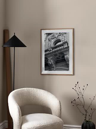 Framed black-and-white photo of an ornate building facade on a beige wall above a white chair