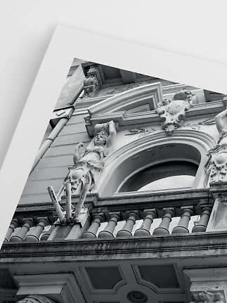 Black-and-white photo of ornate building facade with balcony, arched window and statue, viewed from below