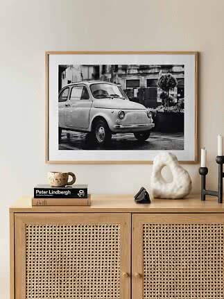 Framed black-and-white print of a classic small car above a wooden cabinet with decor