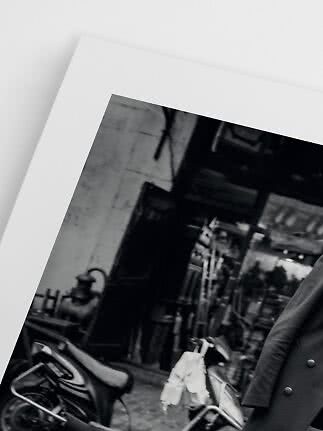 Black-and-white photo print showing a street scene with scooters and a person in a dark coat