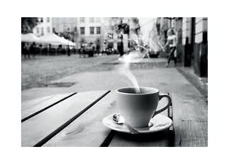 Rygende kaffekop på underkop med ske på træbord ved udendørs café i sort-hvid