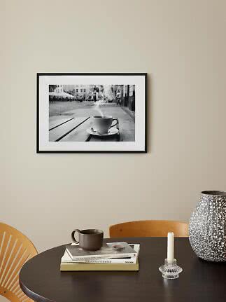 Sort indrammet sort-hvid plakat med dampende kaffekop over rundt bord