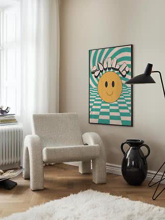 Poster colorato con smiley in cornice nera sopra una poltrona morbida in una stanza luminosa