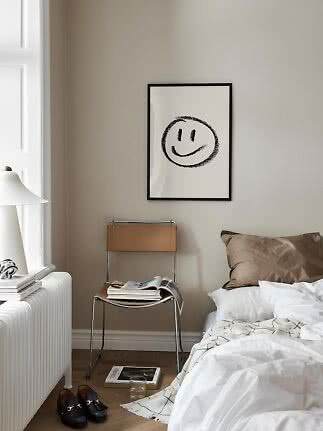 Poster con smiley in cornice nera sopra una sedia in una camera beige
