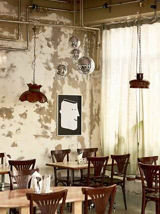 Interno di caffè rustico con sedie in legno, tavolini, sfere a specchio e tubi a vista