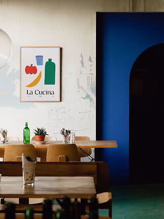 Rustikales Caféinterieur mit Holztischen, Stühlen, Pflanze und farbigem La-Cucina-Poster