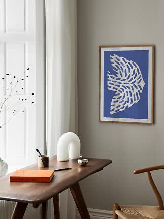 Framed blue and white art print above a wooden desk by a window