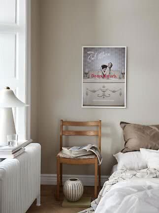 Bedroom with framed poster above wooden chair, bed, white lamp and window