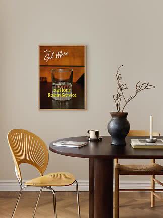 Indrammet hotelplakat med glas og teksten "24-Hour Room Service" over et mørkt spisebord