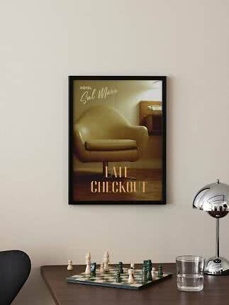 Indrammet vintageplakat med lænestol og teksten "Late Checkout" på lys væg over et skakbræt