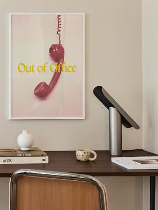Indrammet plakat med pink telefonrør og teksten "Out of Office" over et skrivebord.